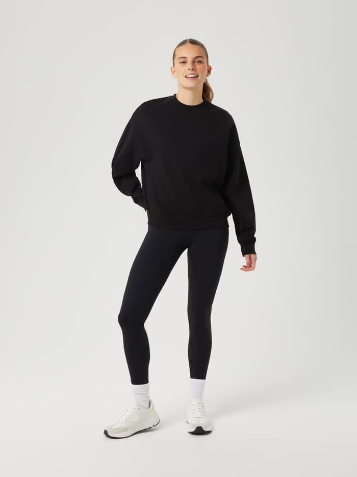 Ganzkörper-Vorderansicht einer Frau im Björn Borg Studio Oversized Crew in Black Beauty (Schwarz) mit Leggings. - Image 3
