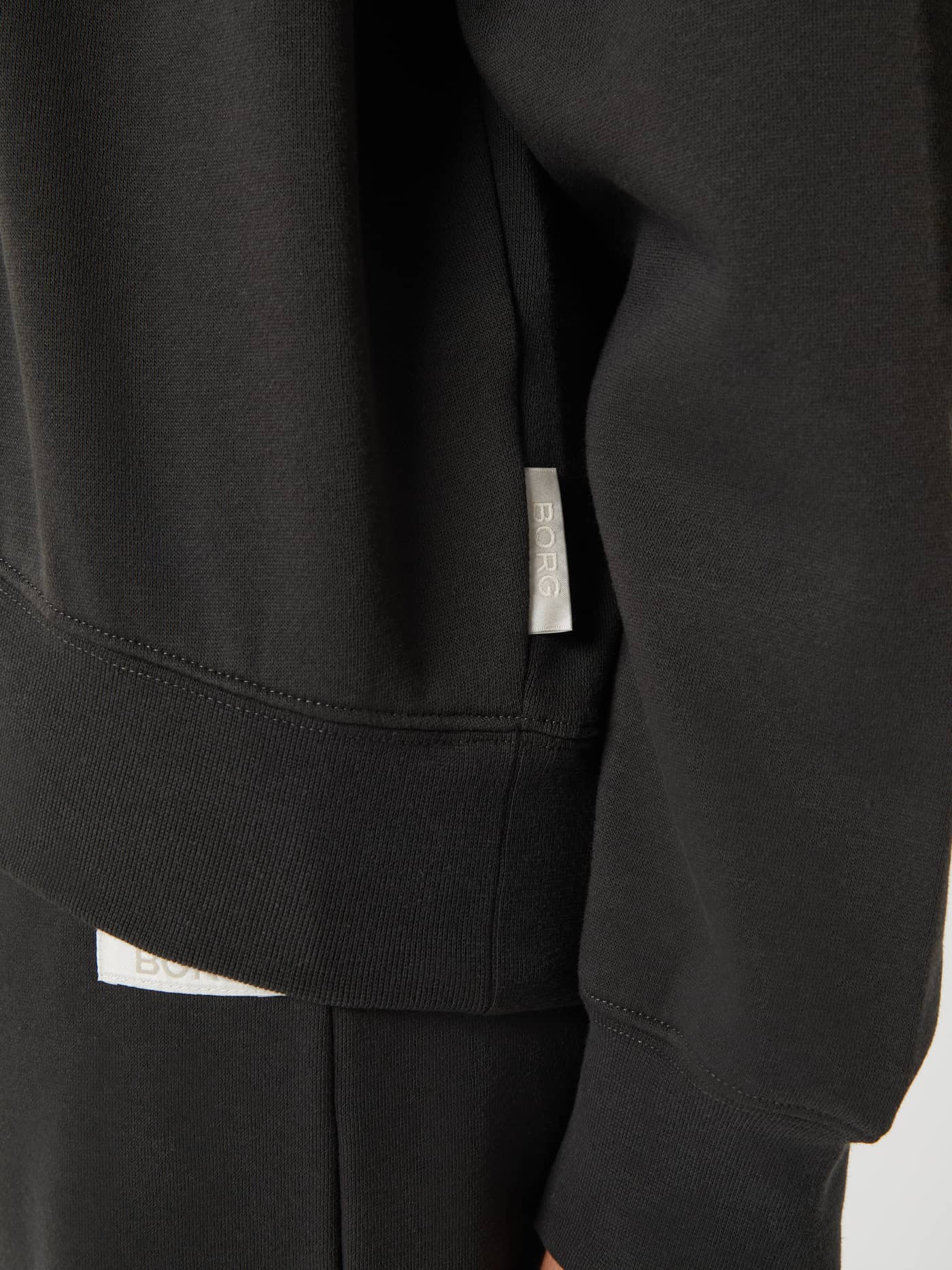 Detailed close-up of the Peat (Green) Studio Oversized Crew, highlighting the white BORG logo label and ribbed hem. - Image 5