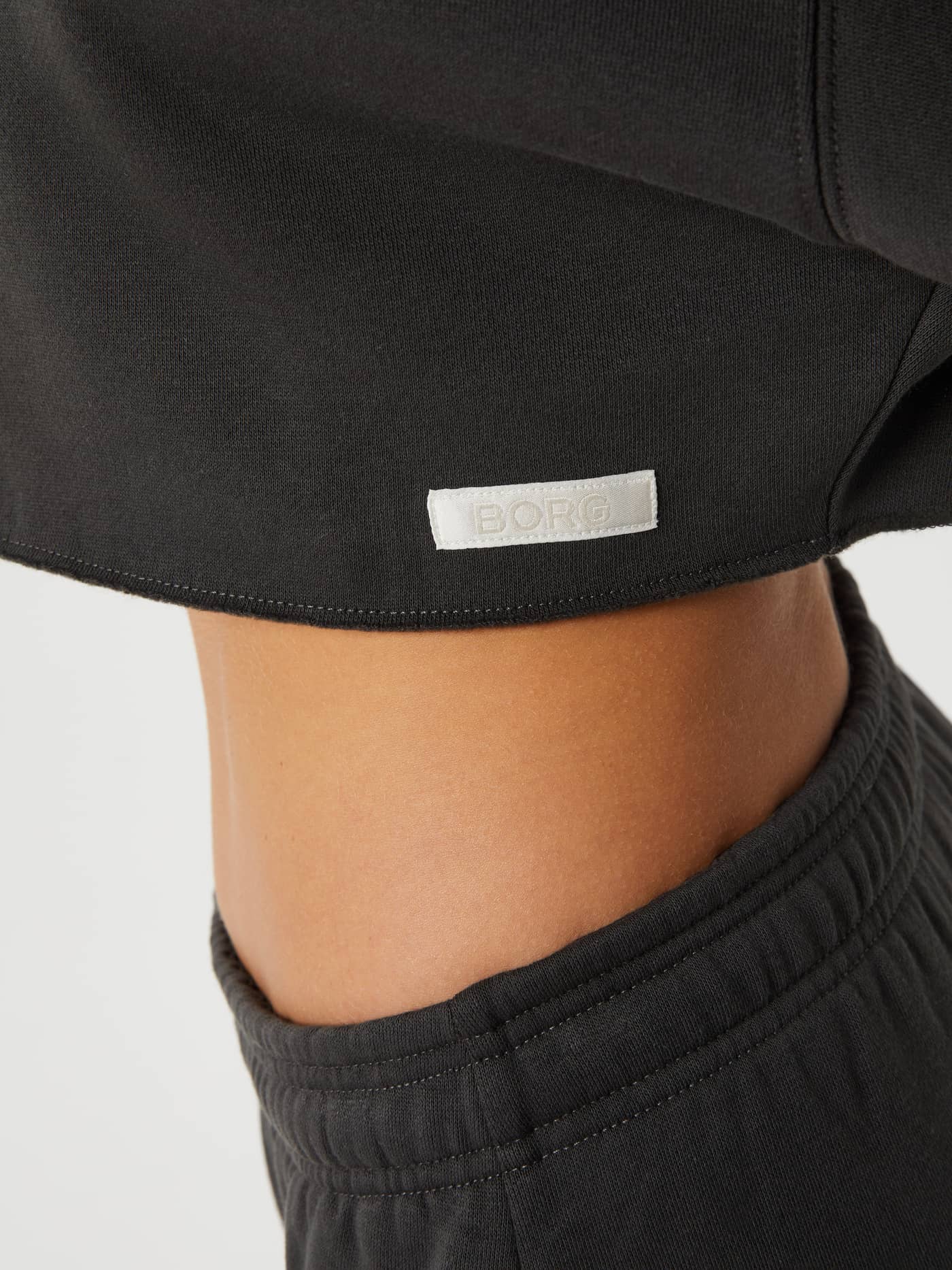 Close-up of the Björn Borg Studio Oversized Cropped Crew in Peat (Green) with raw edges and a white satin logo label. - Image 4