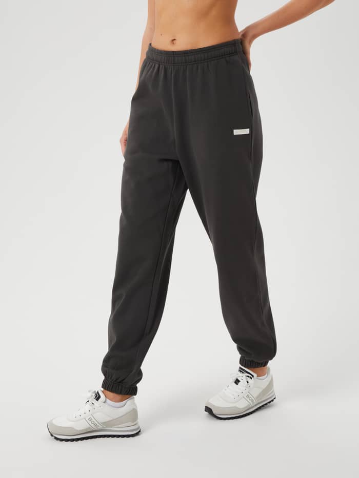 Front view of a model wearing the Studio Oversized Pants in Peat (Green) with oversized fit and white logo for training.