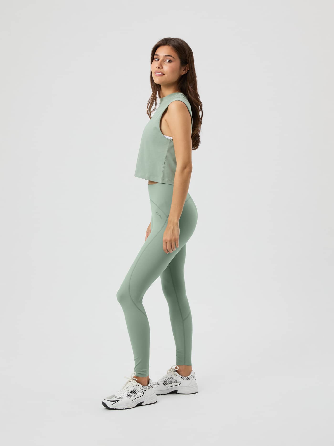 Full length side view of a model wearing the light green Björn Borg Borg Sleek Tights and a matching top in a studio. - Image 1