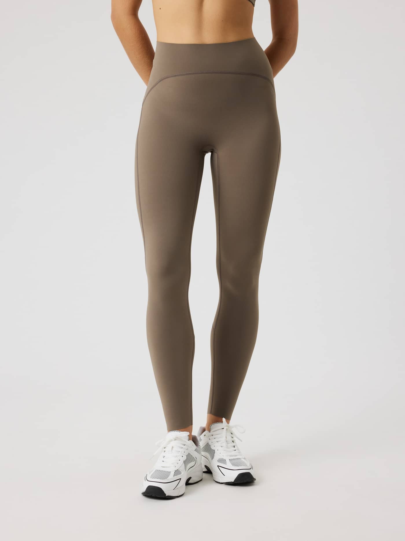 Front view of a model wearing the slim-fit, high-waisted Borg Sleek Tights in Falcon (Brown) for training. - Image 1