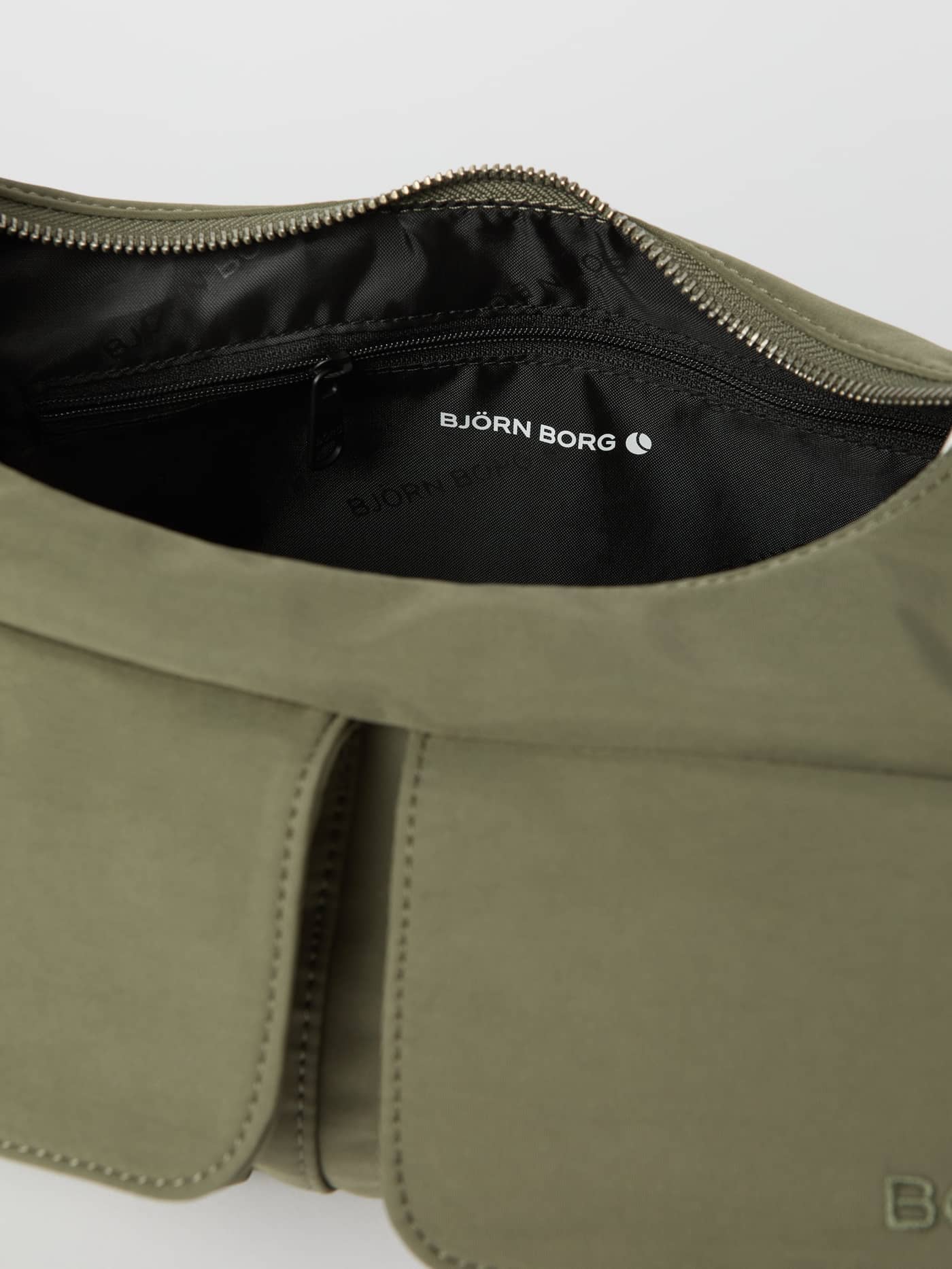 Close-up van de geopende Borg Cargo Shoulder Bag in Vetiver (Groen) met het witte logo en zwarte binnenvoering. - Image 4