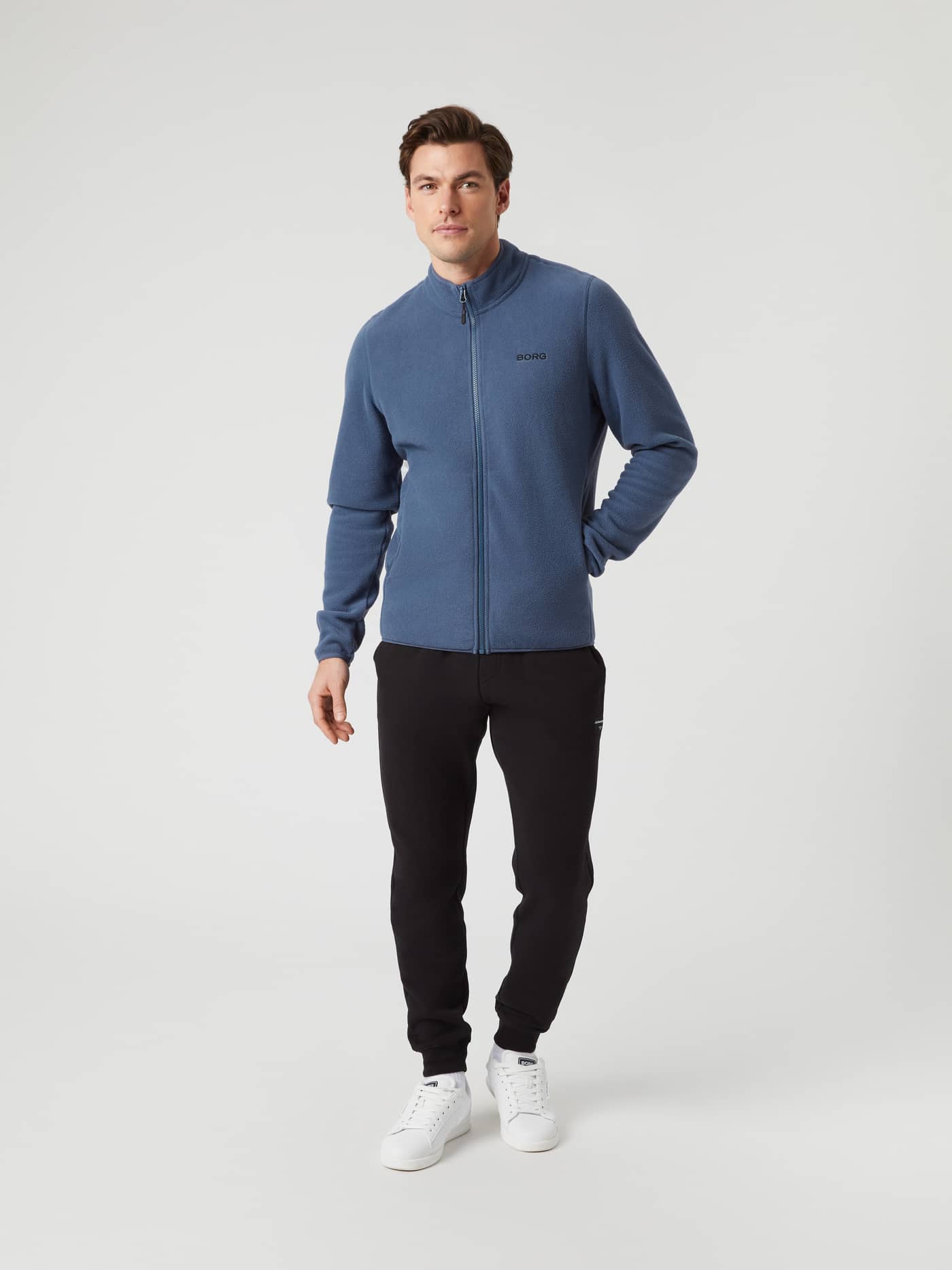 Front view of a model wearing the Borg Full Zip Fleece jacket in Nightshadow Blue with black sweatpants and white shoes. - Image 3