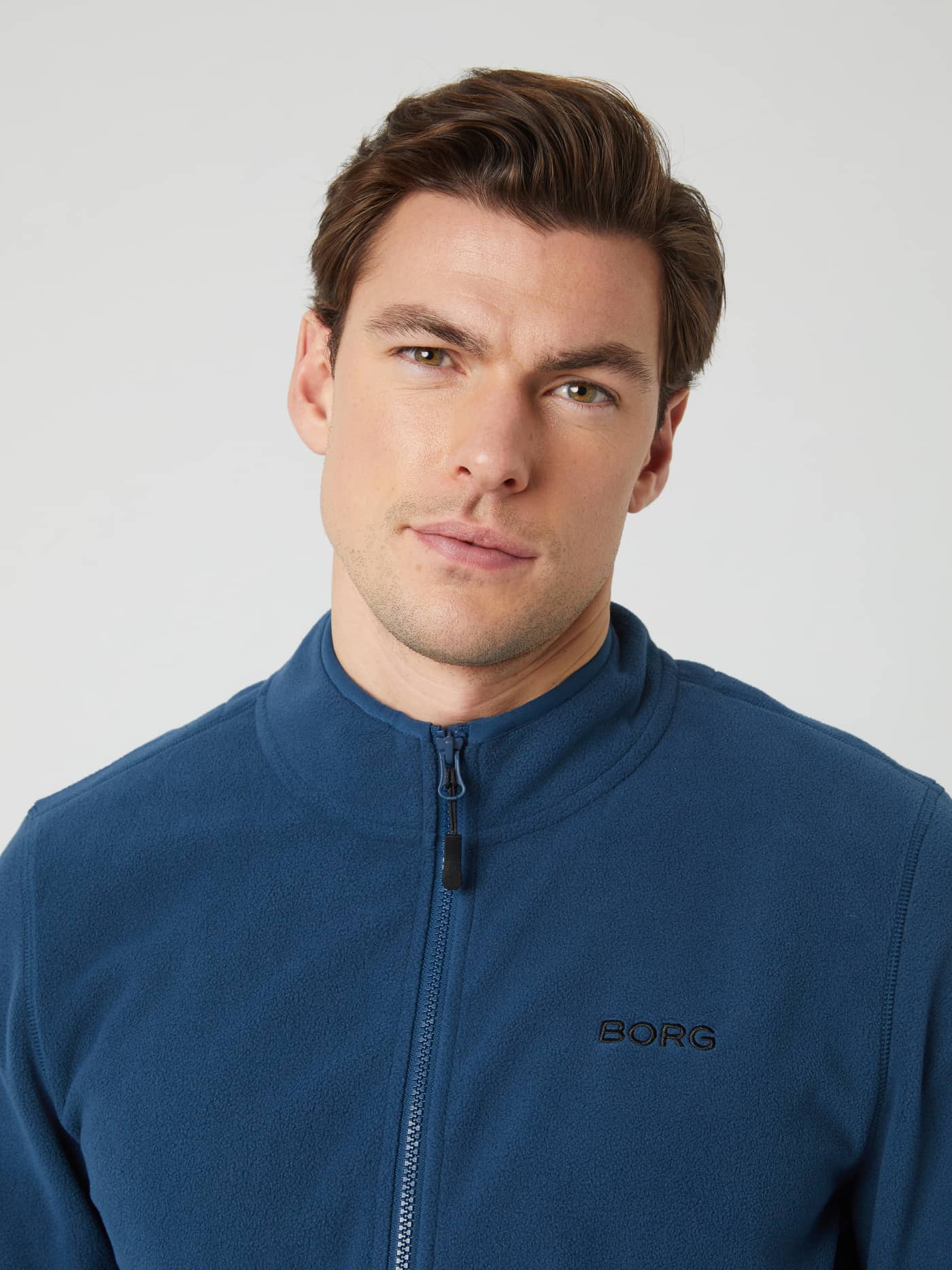 Close-up of a man wearing the blue wing teal Borg Full Zip Fleece, showing the collar and chest logo. - Image 4