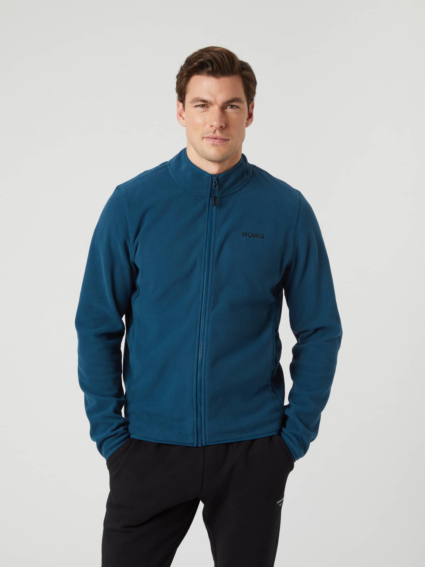 Front view of a model wearing the blue wing teal Borg Full Zip Fleece jacket with hands in pockets. - Image 1