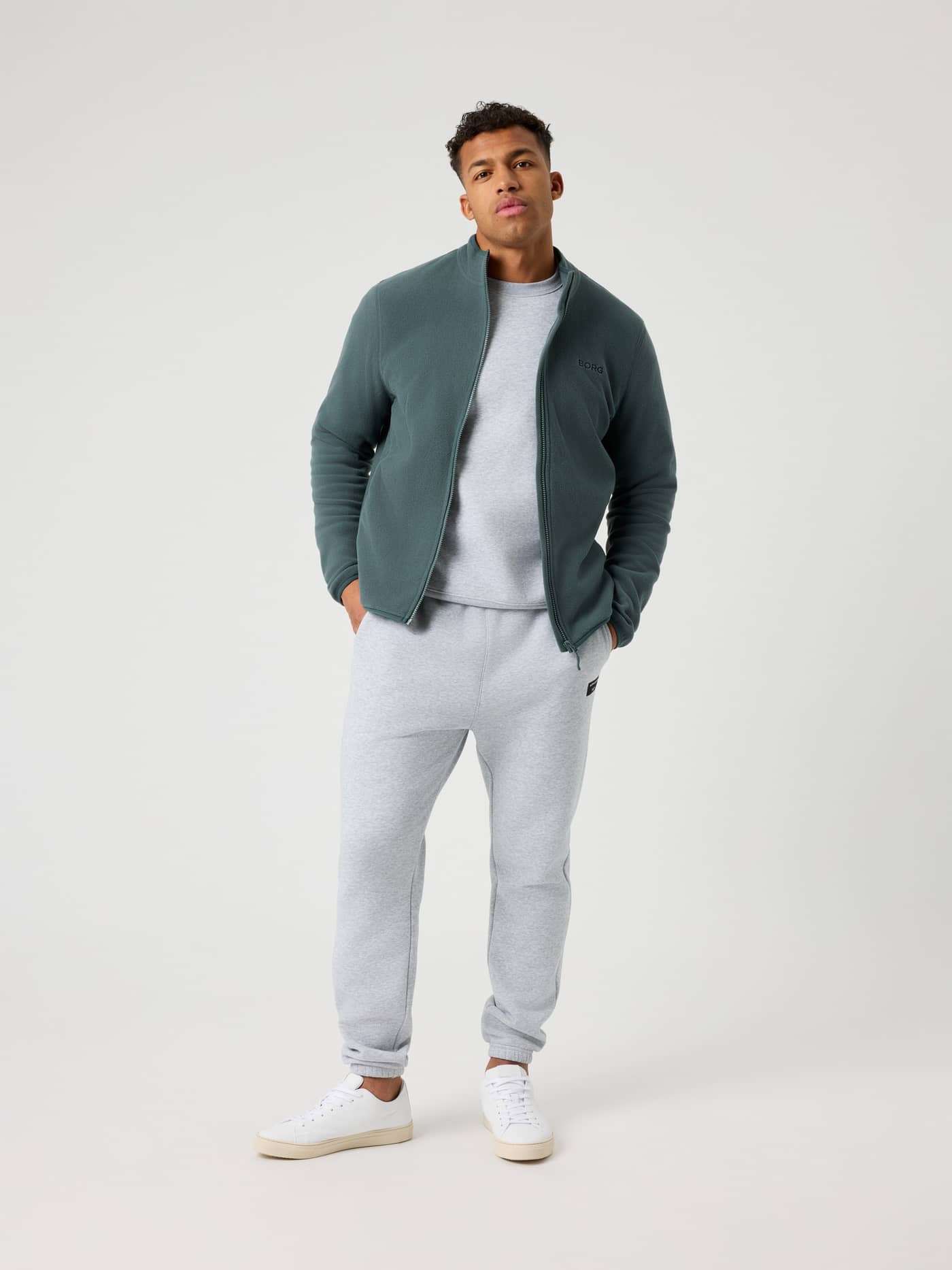 Funktionell Borg Full Zip Fleece i Urban Chic (Grön) med grön logotyp, sedd i helfigur på en man i grå mjukisbyxor. - Image 3