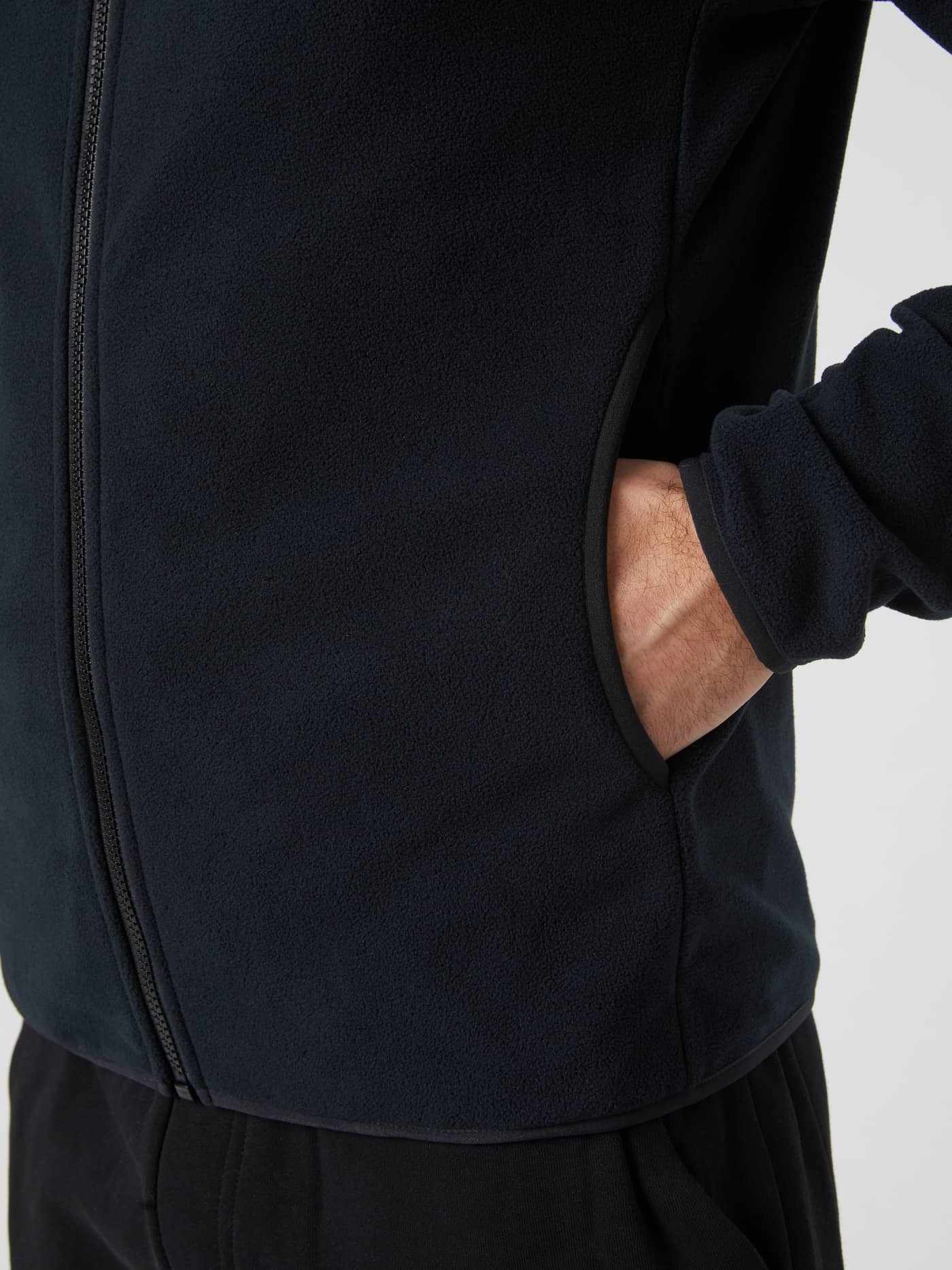 A close-up view of a model's hand inside the side pocket of the black Borg Full Zip Fleece jacket. - Image 5