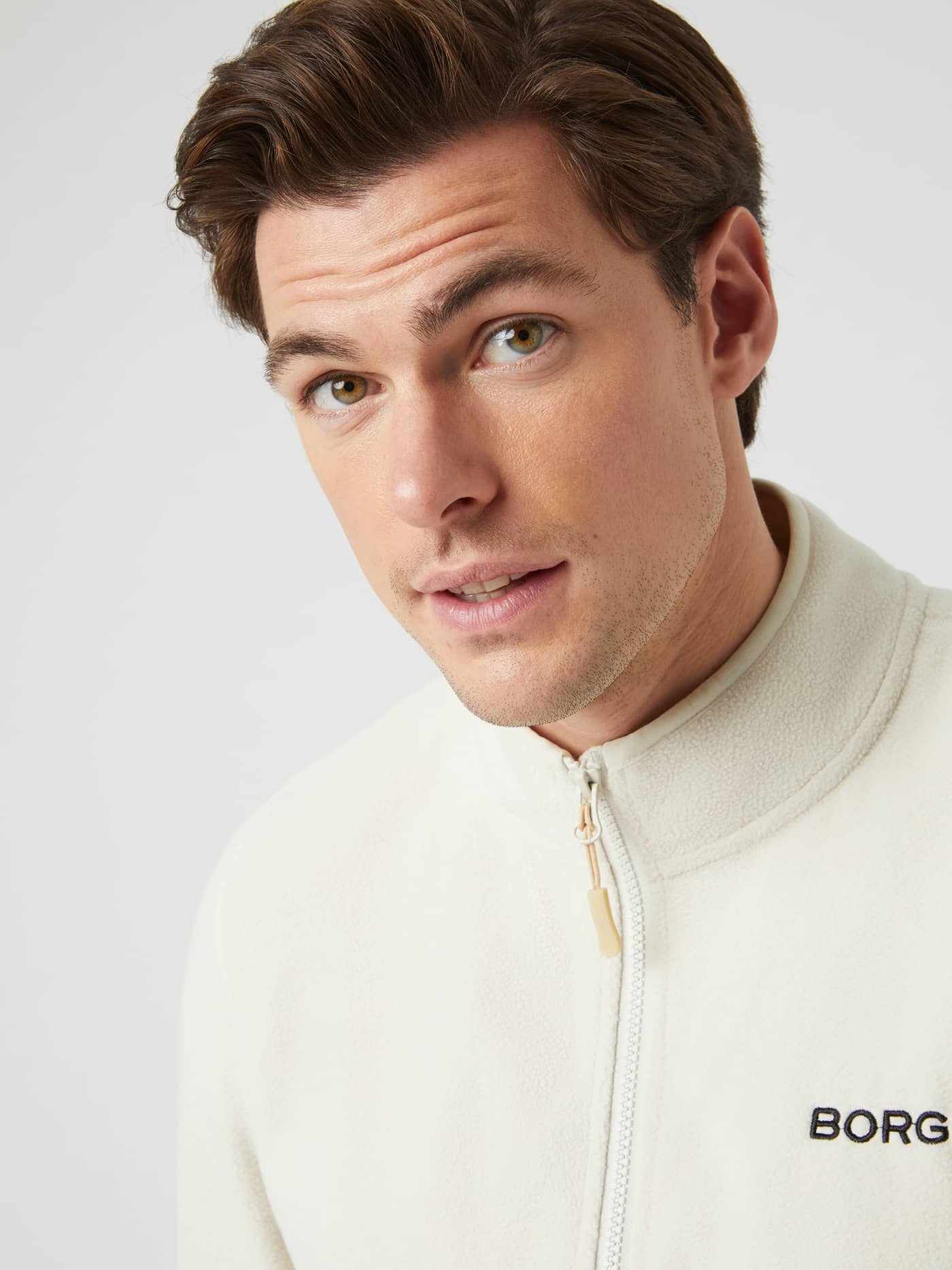 Close-up of a model wearing the silver birch Borg Full Zip Fleece, showing the high collar, zipper, and chest logo. - Image 5