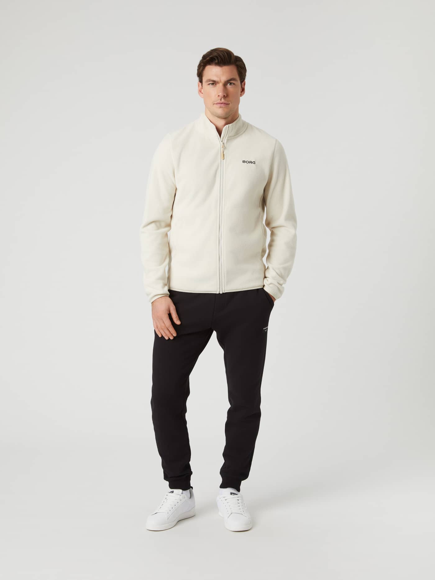 Male model wearing the Silver Birch Borg Full Zip Fleece, black sweatpants, and white sneakers, seen from the front. - Image 4