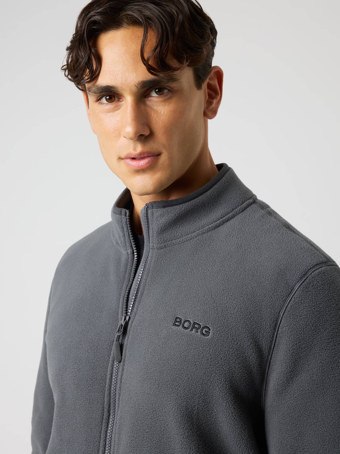 Close-up of a model wearing the Borg Full Zip Fleece in Asphalt (Black) with a black chest logo for training. - Image 4