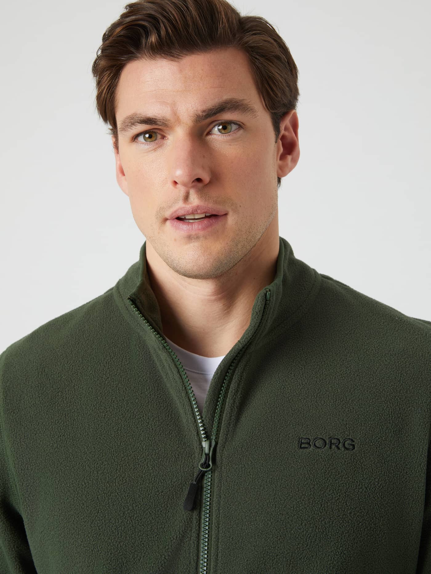 Close-up of a model wearing the dark green Borg Full Zip Fleece, showing the high collar, zipper, and chest logo. - Image 4
