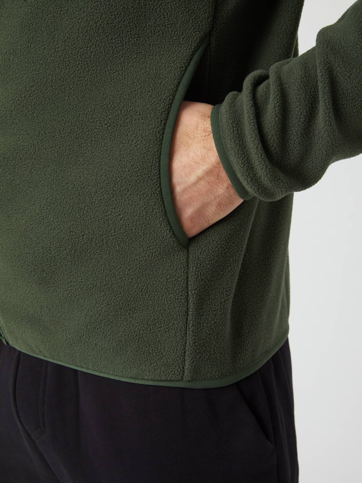 Close-up of a hand in the side pocket of the men's Borg Full Zip Fleece jacket in Duffel Bag green. - Image 5