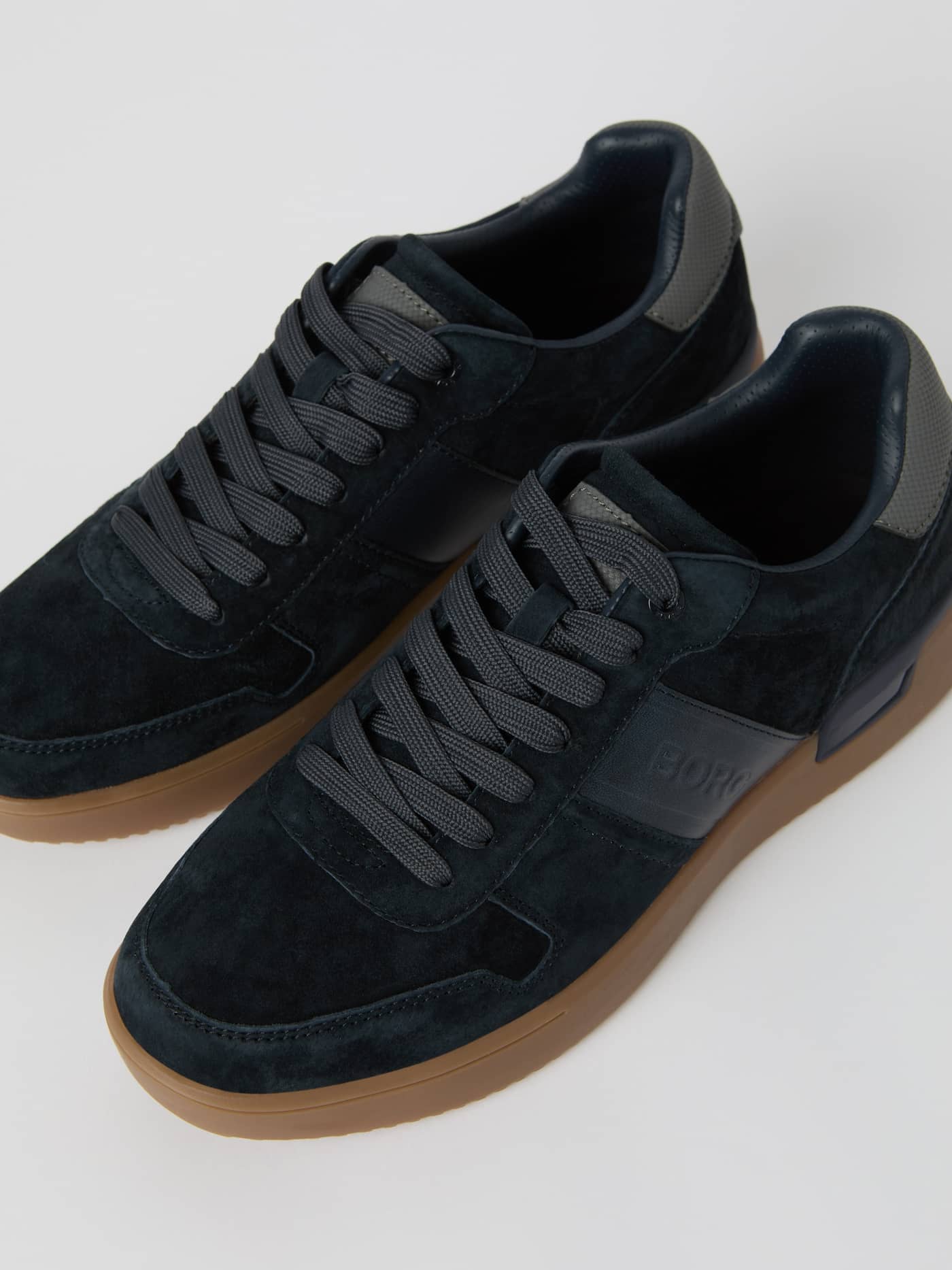 Detailed view of the navy Men's Spin Sneakers featuring soft suede leather, a functional gum rubber sole, and embossed logos. - Image 3