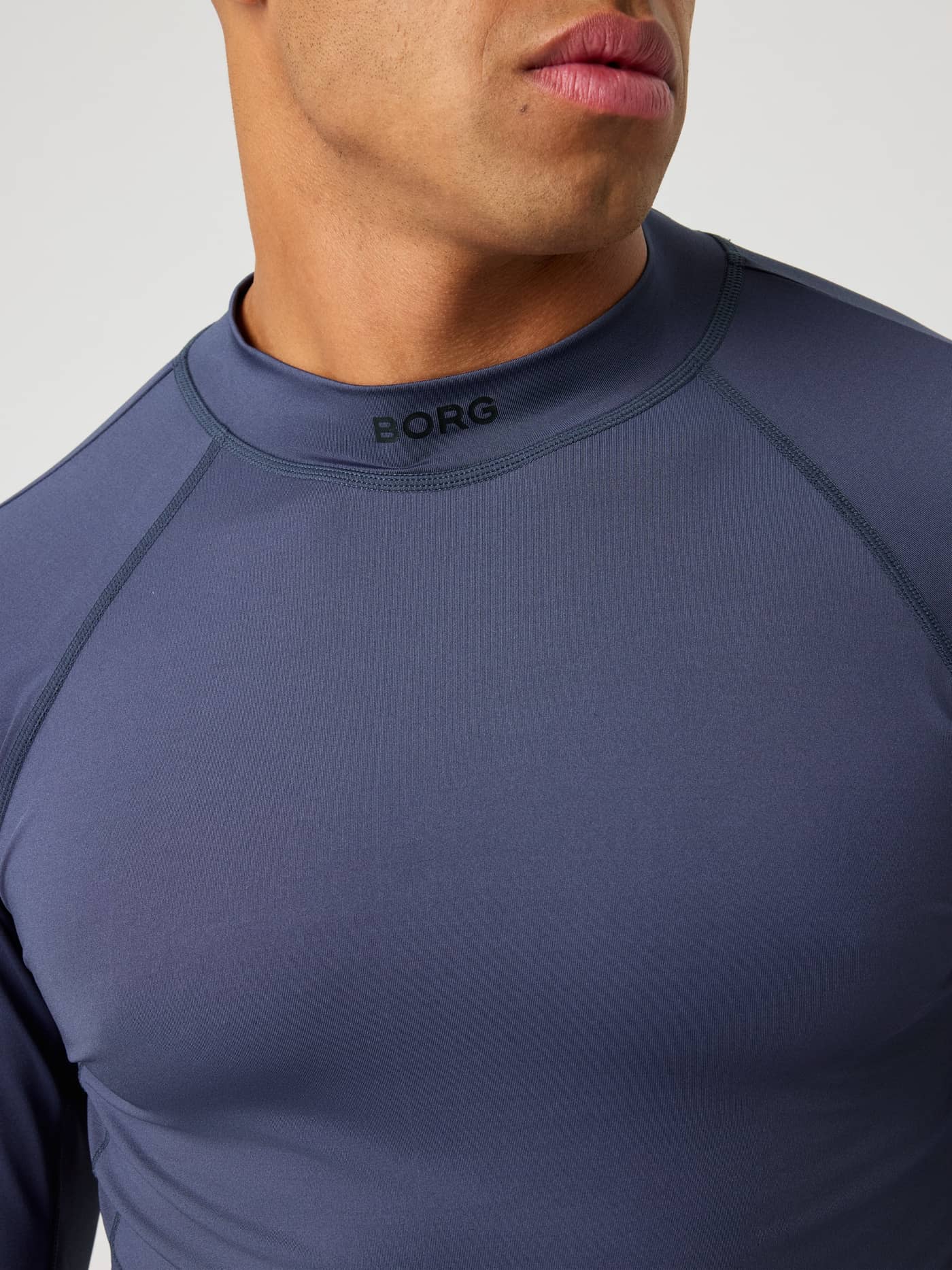 Nahaufnahme des Borg Mock Neck Ls T-Shirt in Odyssey Gray (Blau) mit schwarzem Logo für Training-Performance. - Image 5