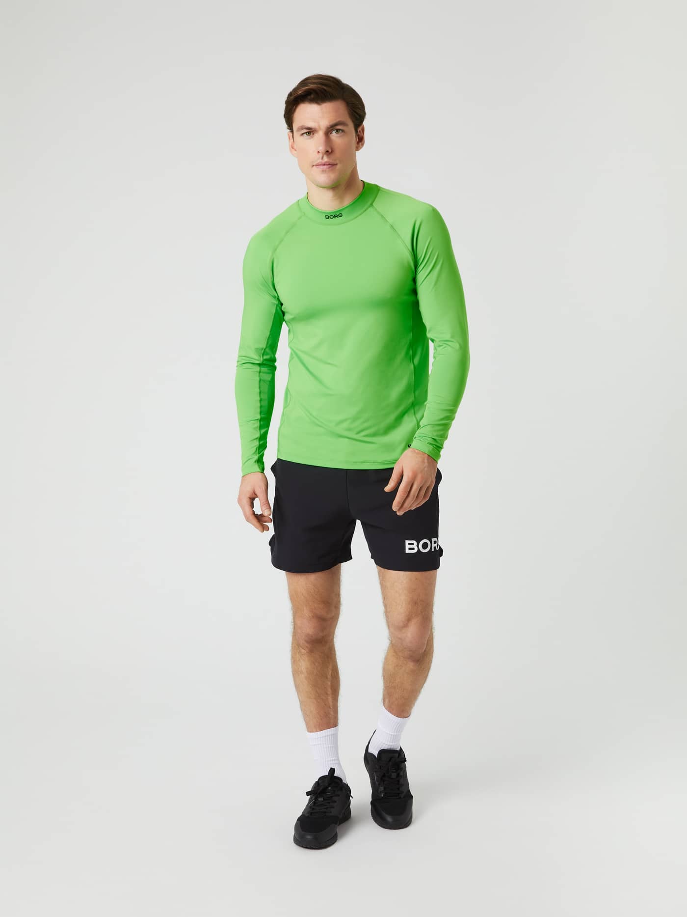 Front view of a model wearing the green Borg Mock Neck Long-Sleeved T-shirt paired with black shorts. - Image 2