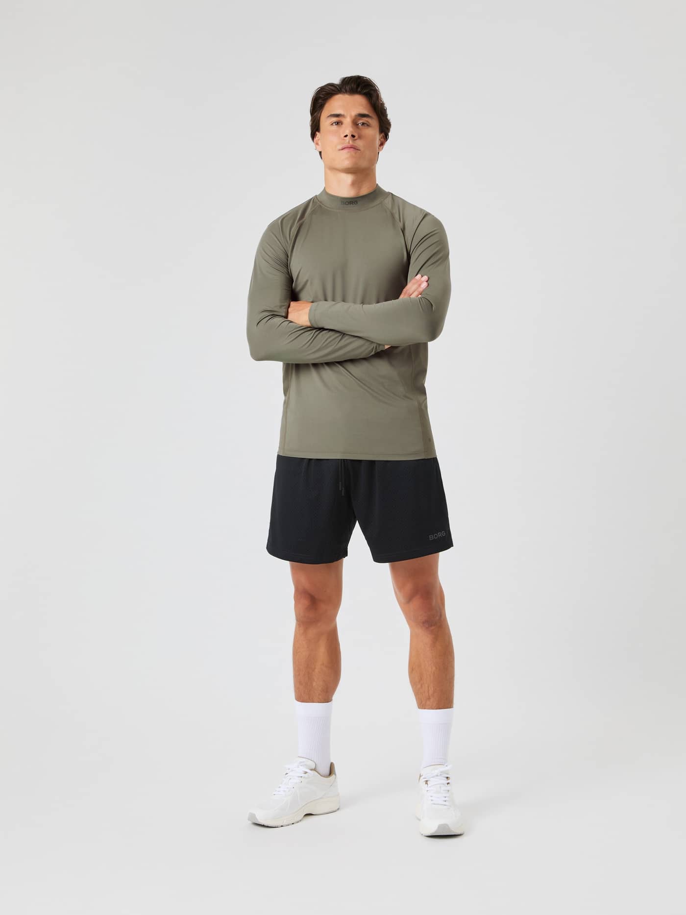 Full body front view of a model wearing the Borg Mock Neck LS T-shirt in dusty olive, paired with black shorts. - Image 3
