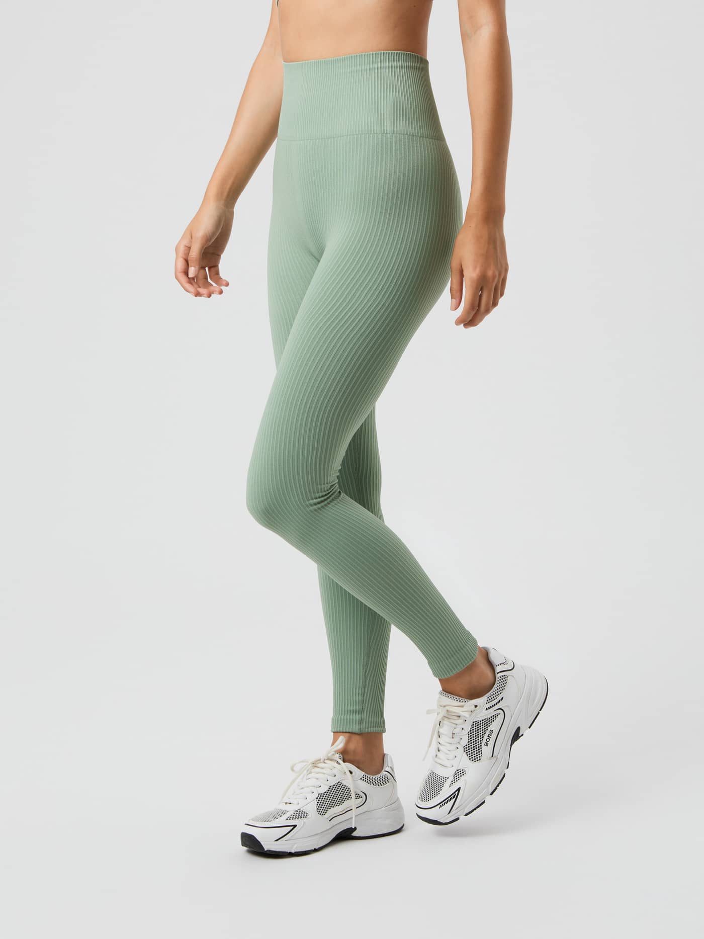 Model from the side wearing the light green, high-waisted Björn Borg Studio Seamless Ribbed Tights. - Image 2