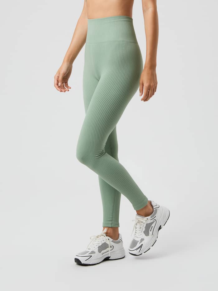 Seitenansicht eines Models in den hochtaillierten Studio Seamless Ribbed Tights in Lily Pad (Grün) fürs Training. - Image 2