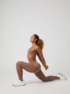 Studio Seamless Ribbed Tights en sport-bh in Acorn (Bruin) gedragen in een lunge-houding, ideaal voor training. - Image 1