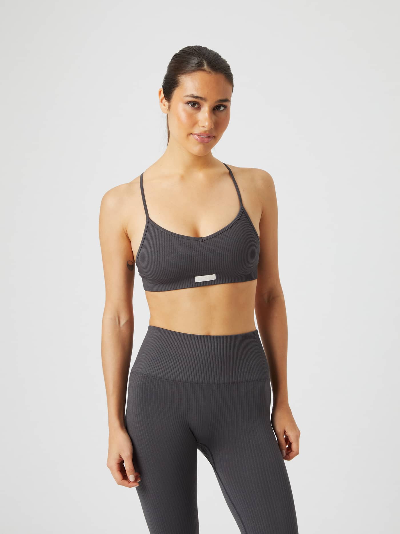 Studio Seamless Ribbed Strap Bra in Grey on a model, featuring a ribbed texture, light logo and a stylish fit for training. - Image 1