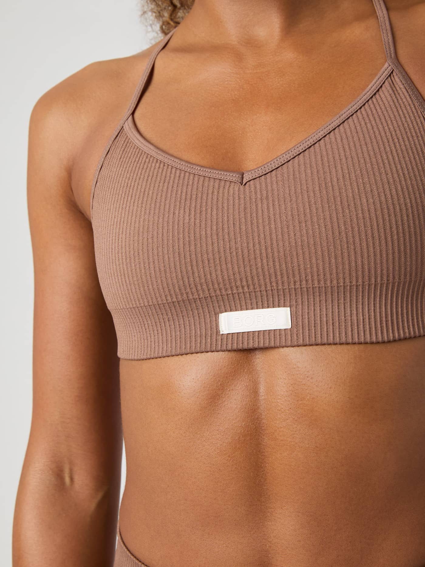 Gros plan de face du Studio Seamless Ribbed Strap Bra en Acorn (Marron) avec logo blanc et coupe côtelée. - Image 3