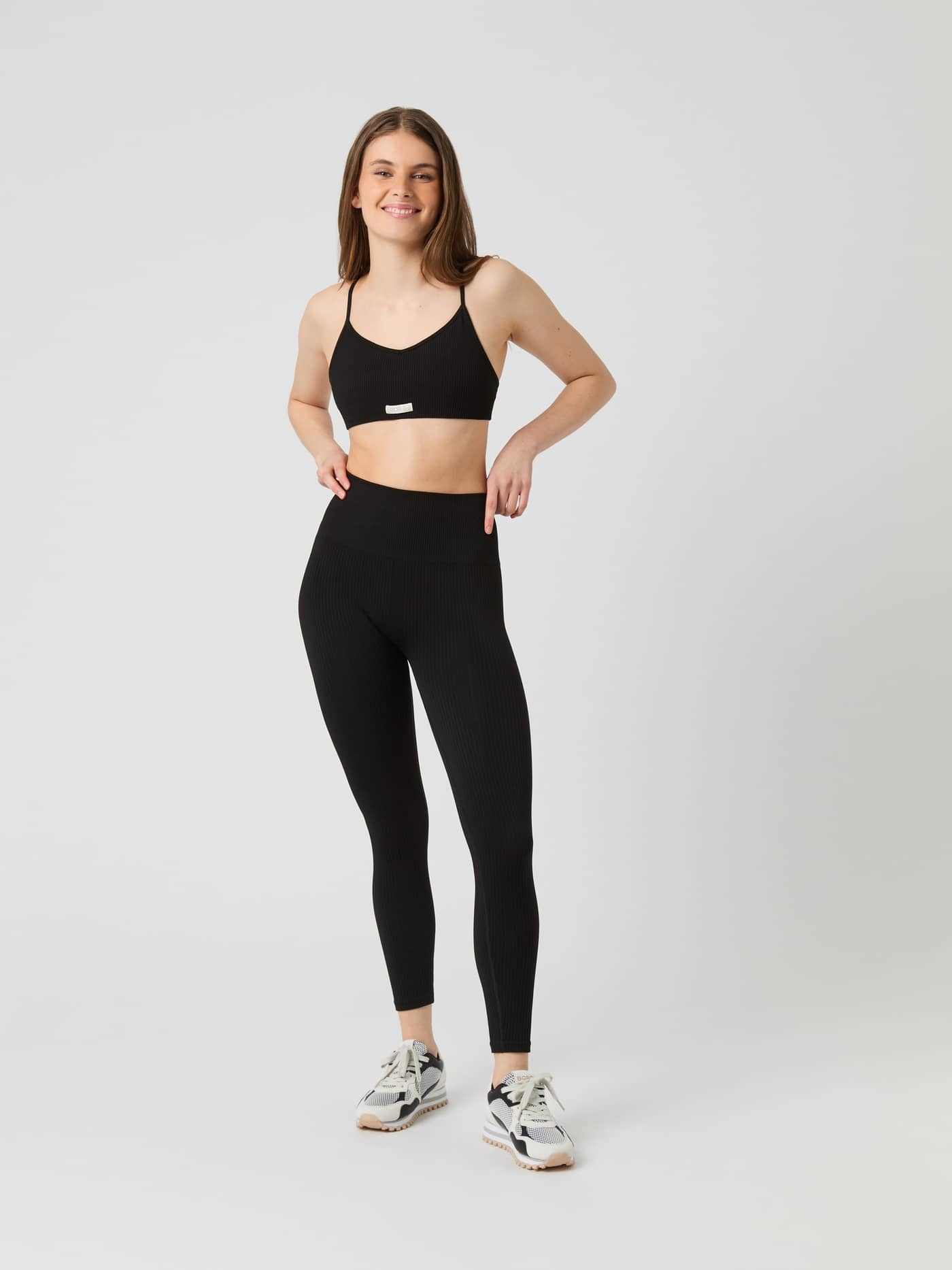 Vue de face d'une femme en Studio Seamless Ribbed Strap Bra Noir sans coutures avec logo blanc offrant une coupe performante. - Image 3