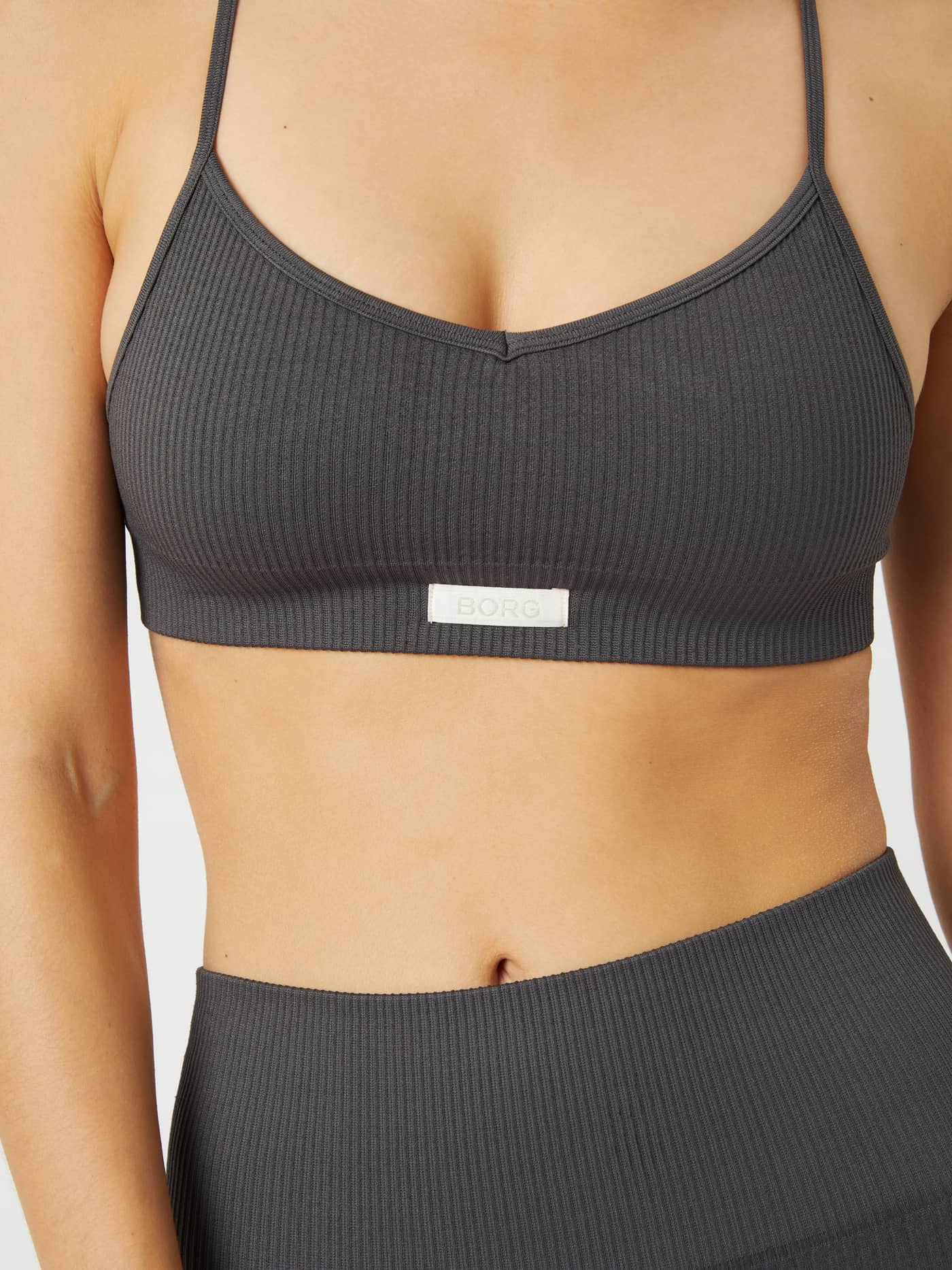 Close-up front view of a woman wearing the grey Studio Seamless Ribbed Strap Bra featuring a white BORG logo. - Image 3