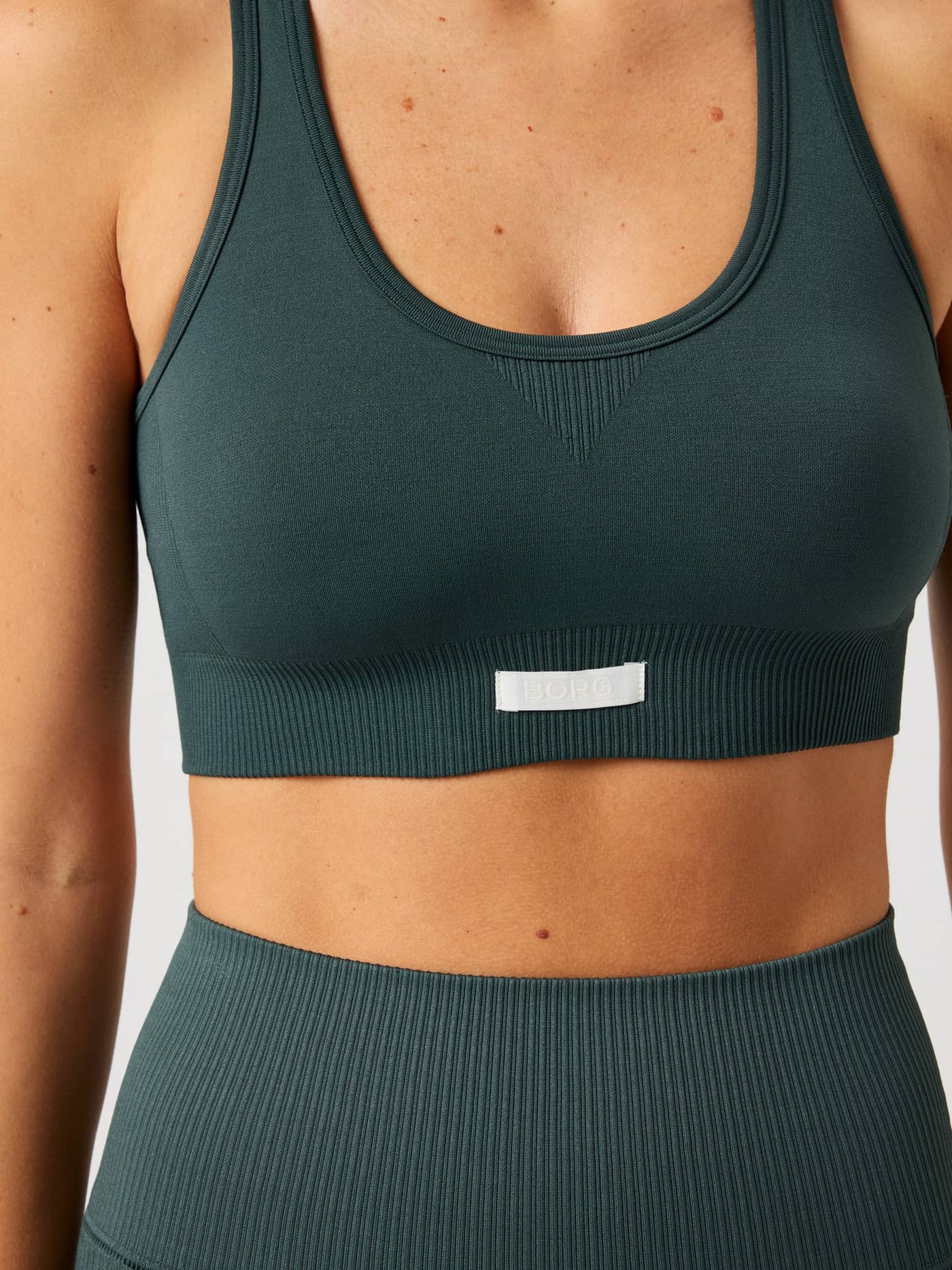 Close-up of the green Studio Seamless Low Sports Bra for training, featuring a seamless fit and white woven logo label. - Image 5