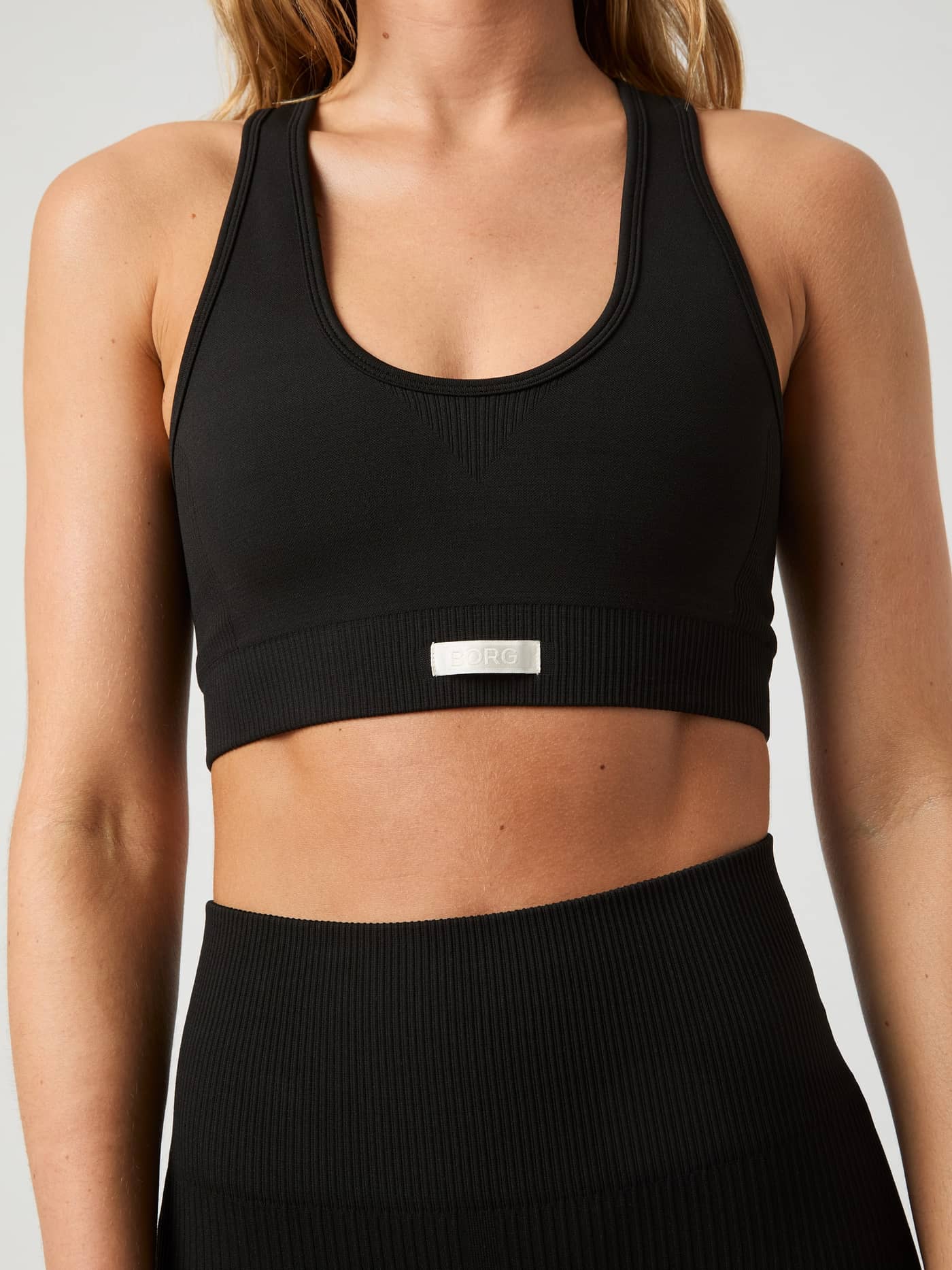 Close-up front view of a model wearing the black Björn Borg Studio Seamless Low Sports Bra, showing the ribbed texture. - Image 2