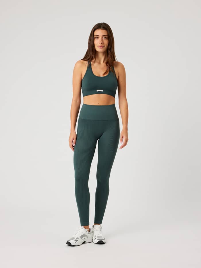 Studio Seamless Low Sports Bra i Urban Chic (Grön) sedd framifrån, en sömlös sport-bh med vit logoetikett för träning. - Image 3