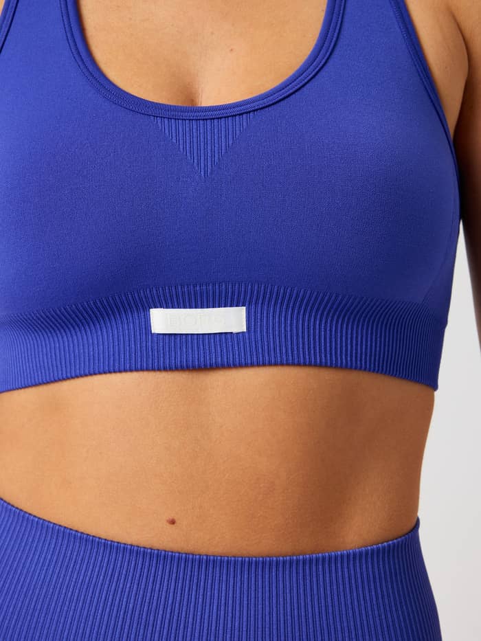 Närbild på Studio Seamless Low Sports Bra i Clematis Blue (Blå) för träning med en vit logoetikett. - Image 5