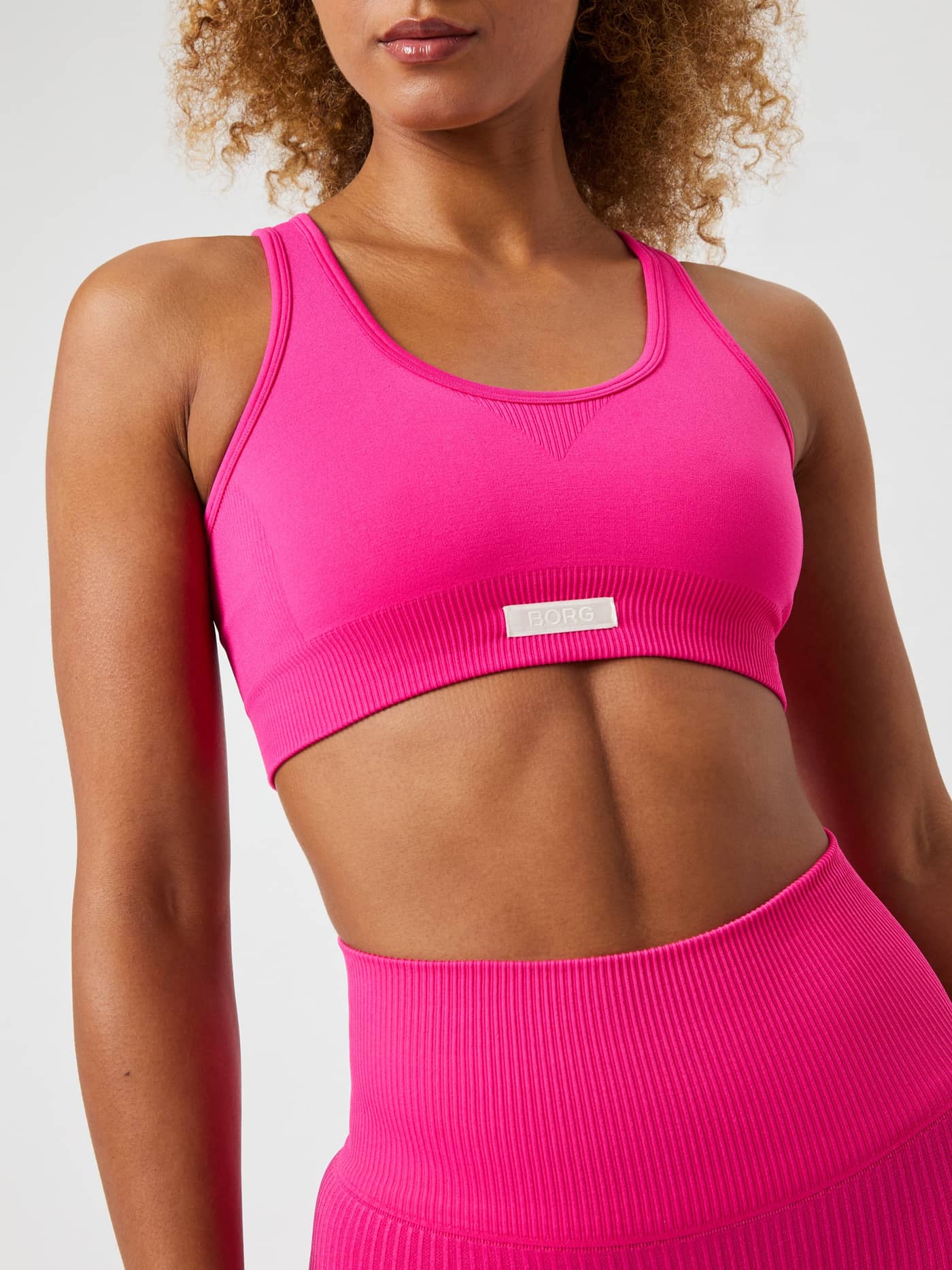 Gros plan de face du Studio Seamless Low Sports Bra Pink Glo (Rose) avec logo blanc, idéal pour l'entraînement. - Image 5