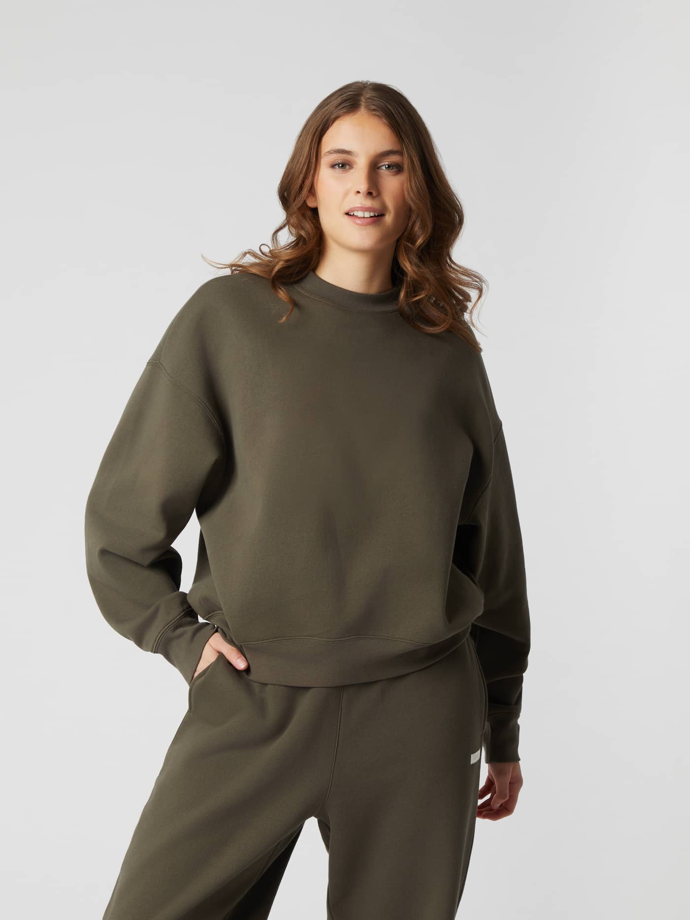 Front view of a woman wearing the Studio Oversized Crew in Tarmac (Brown), an organic cotton sweatshirt with a relaxed fit. - Image 1