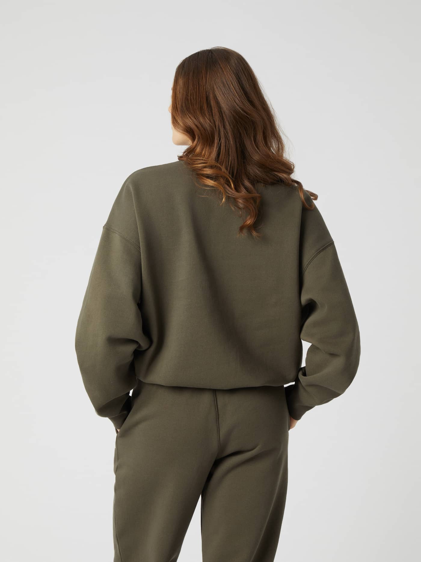 Back view of a woman wearing the Studio Oversized Crew in Tarmac (Brown), in organic cotton with a stylish, oversized fit. - Image 3