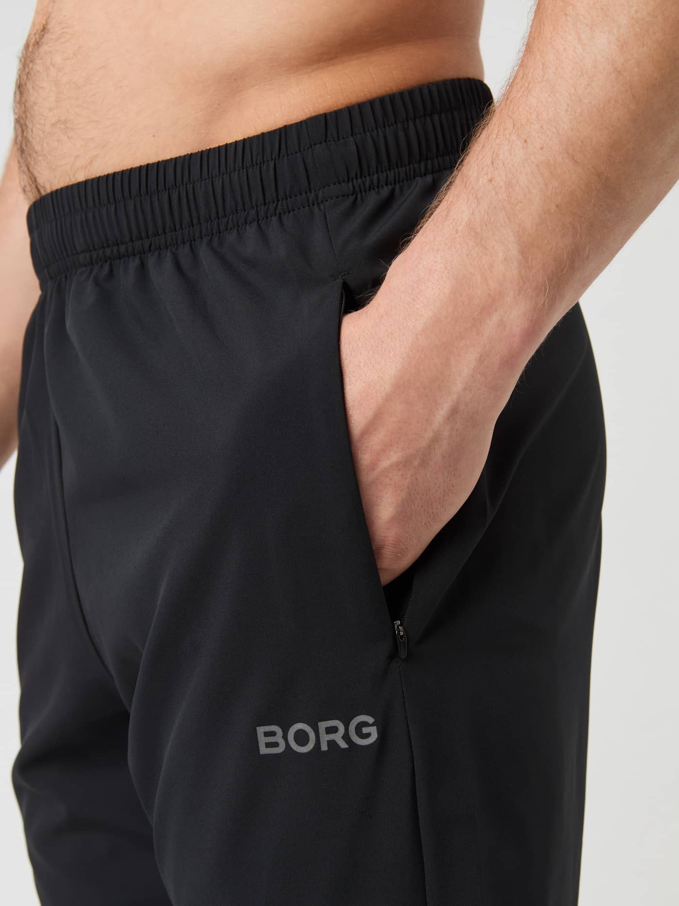 Close-up of the Borg Running Pants in Black Beauty (Black) showing a zippered pocket and the reflective BORG logo. - Image 5