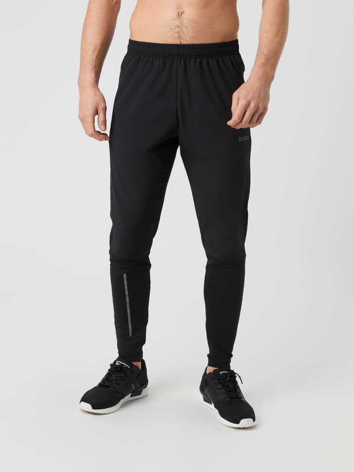 Front view of a man wearing the Borg Running Pants in Black Beauty (Black) with a tonal logo and reflective details.