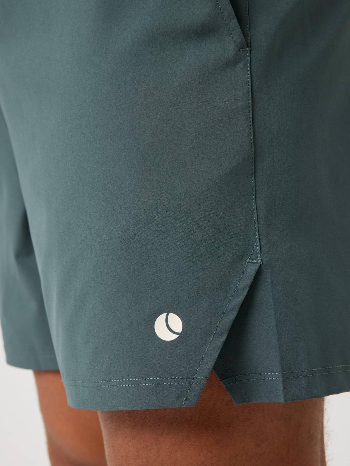 Närbild på Ace Racquet Shorts 7 Inch i Urban Chic (Grön) för tennis med sidslits och vit tennisbollslogotyp. - Image 4