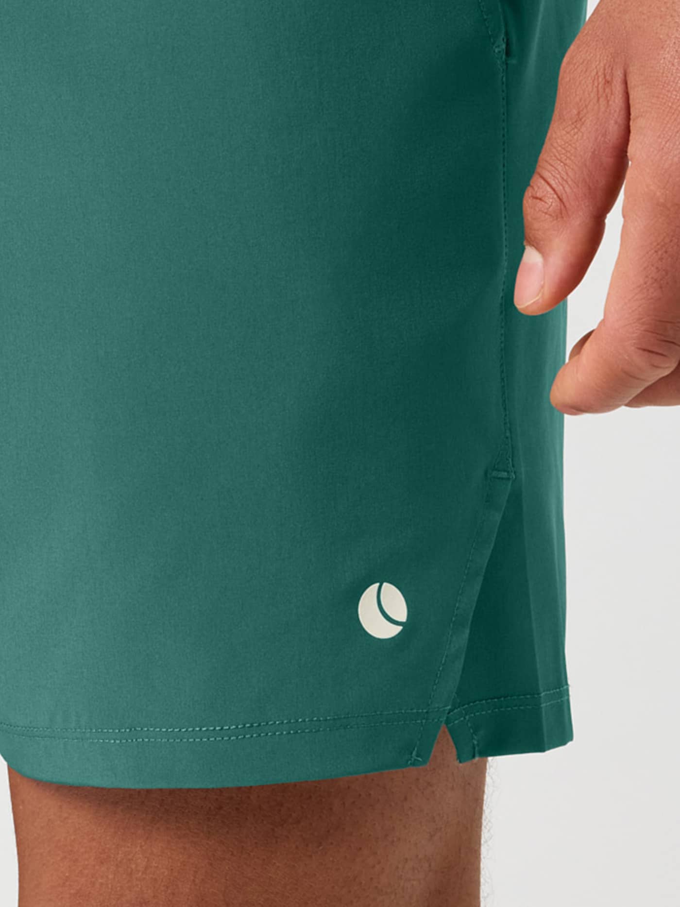 Close-up of the Ace Racquet Shorts 7 Inch in Mallard Green (Green) for tennis, showing a side slit and white ball logo. - Image 4