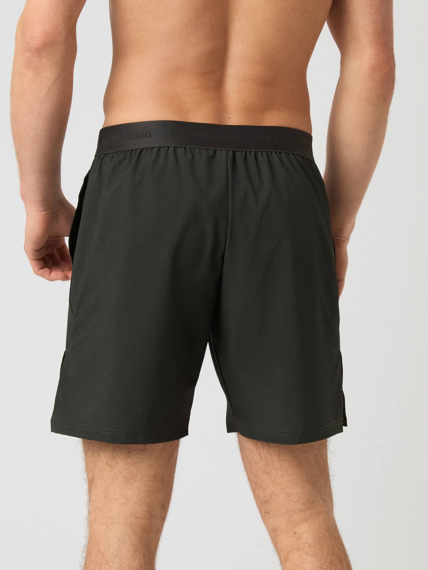 Back view of a man wearing Björn Borg Ace Pro Shorts 7 Inch in Peat (Green) with a black branded waistband for tennis. - Image 3