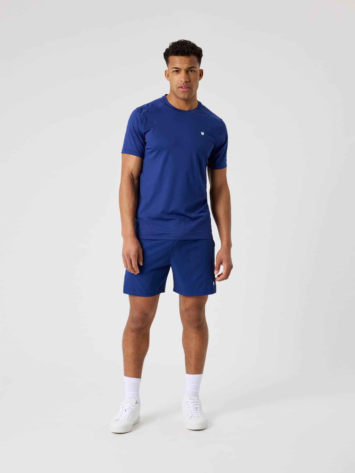 Ace Sports Shorts 8 Inch i Blue Depths (blå) sett forfra på en mann, funksjonell tennisshorts med hvit logo. - Image 3