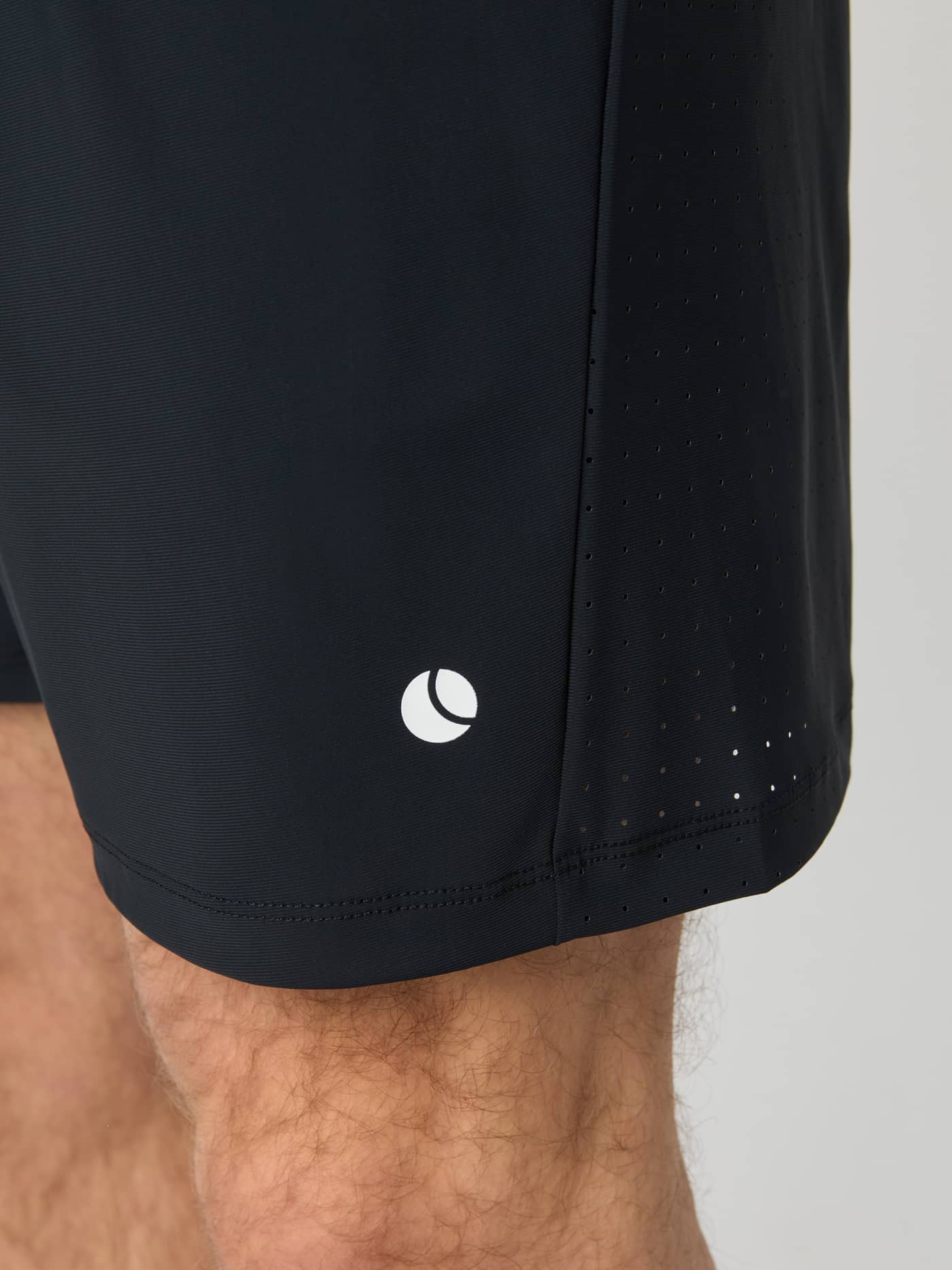 Gros plan du Ace Sports Shorts 8 inch en Black Beauty (Noir) avec logo balle de tennis et empiècement perforé. - Image 5