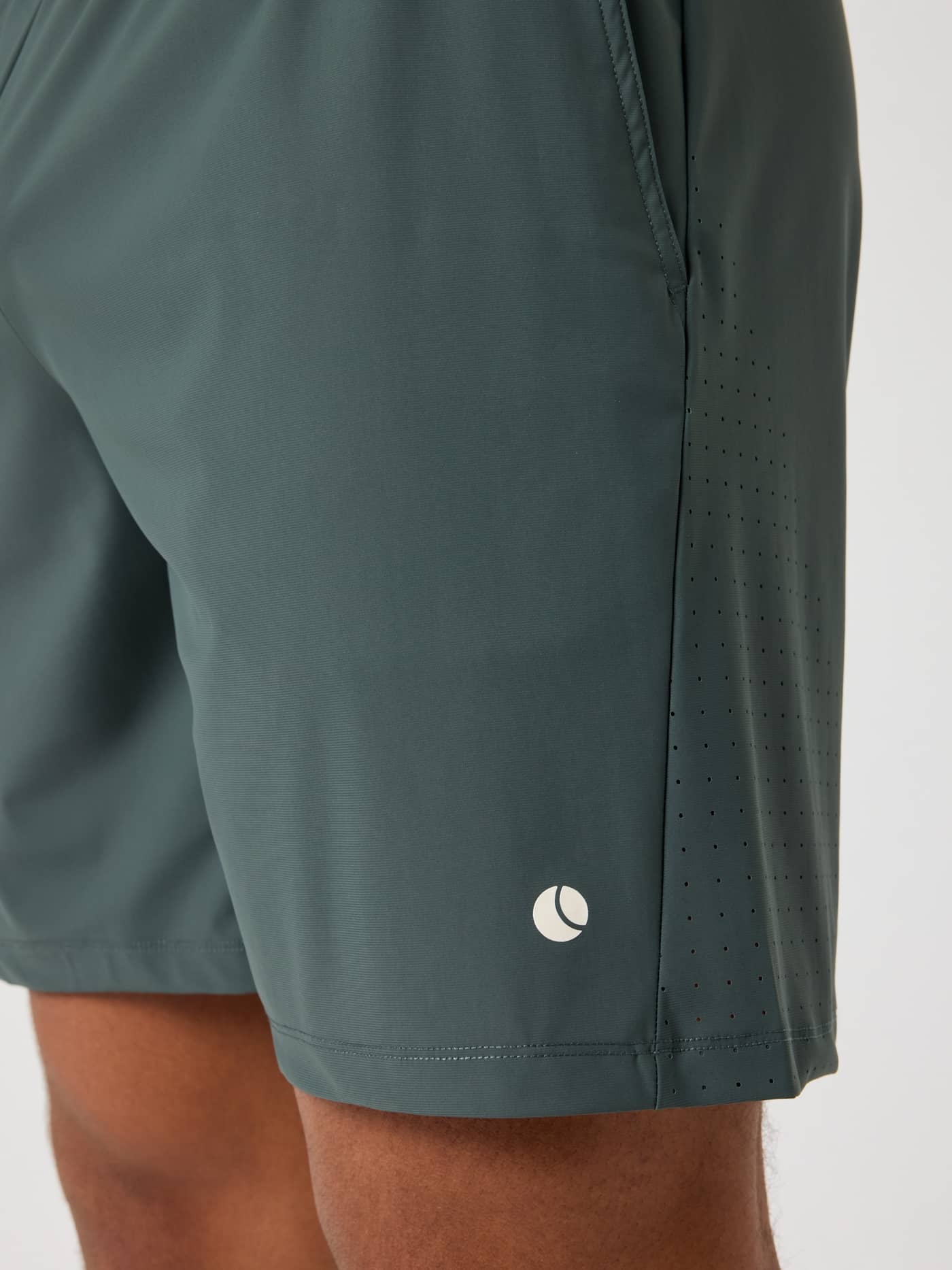 Side detail of the Ace Sports Shorts 8 Inch in Urban Chic (Green) with laser-cut vents and a white tennis ball logo. - Image 4