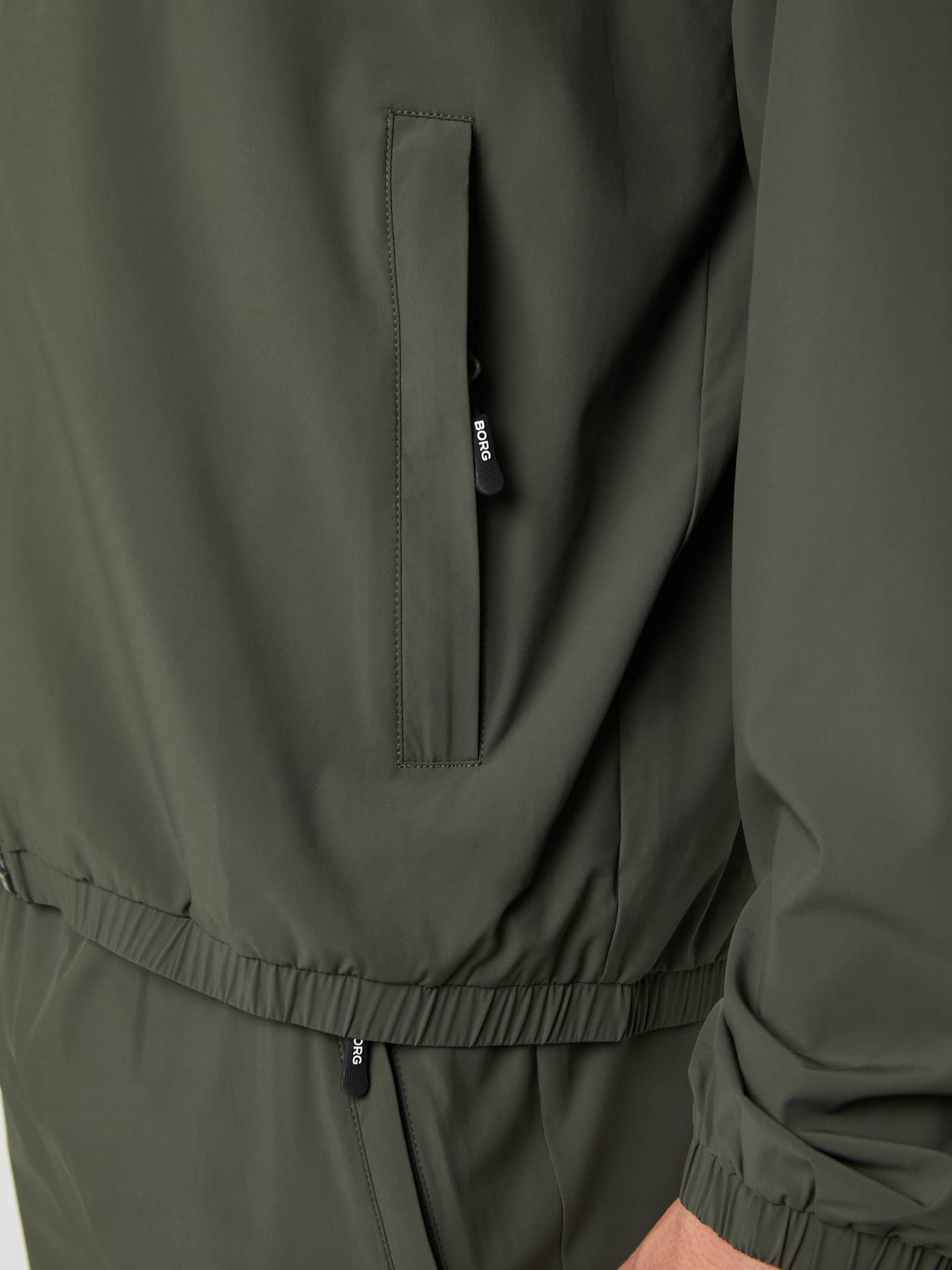 Ace Track Jacket in Peat (Groen) met een close-up van een ritszak en wit BORG-logo, ideaal voor tennis. - Image 4