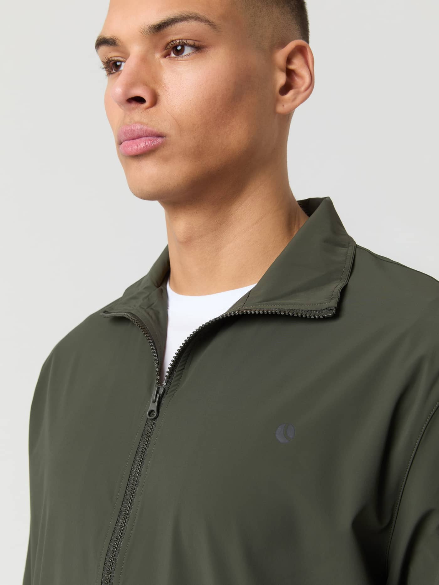 Close-up van een man in het Ace Track Jacket in Peat (Groen) met een zwart tennisballogo voor tennis. - Image 5