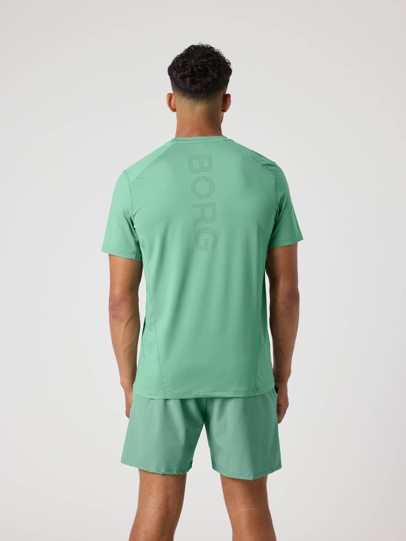 Back view of a man in the Björn Borg Ace Mesh Panel T-Shirt in Malachite Green (Green) with a perforated logo for tennis. - Image 2