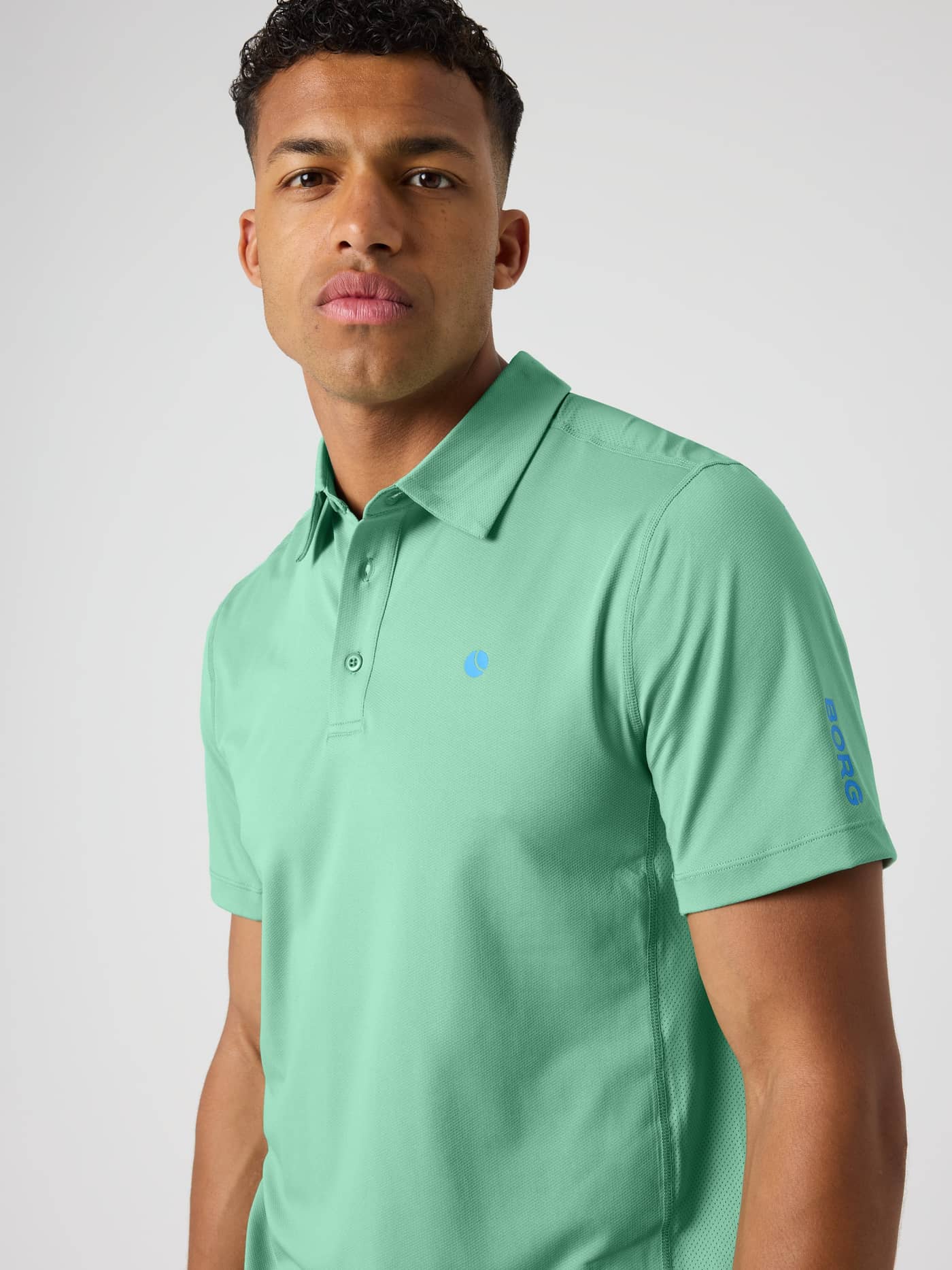 Front view of a man in the Malachite Green (Green) Ace Mesh Panel Polo Shirt with mesh details and a blue tennis ball logo. - Image 5