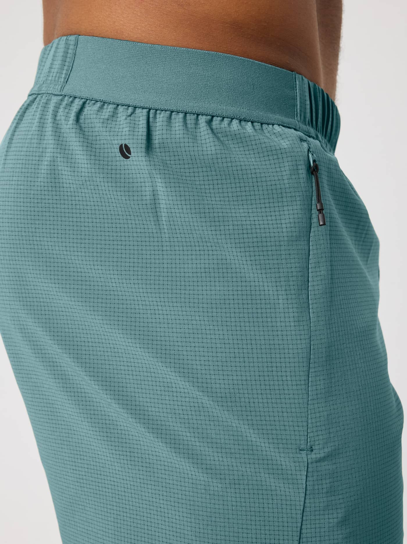 Side view of a man in the Borg Zip Shorts 7 Inch in Balsam Green (Green) with a black tennis logo and perforated weave. - Image 5