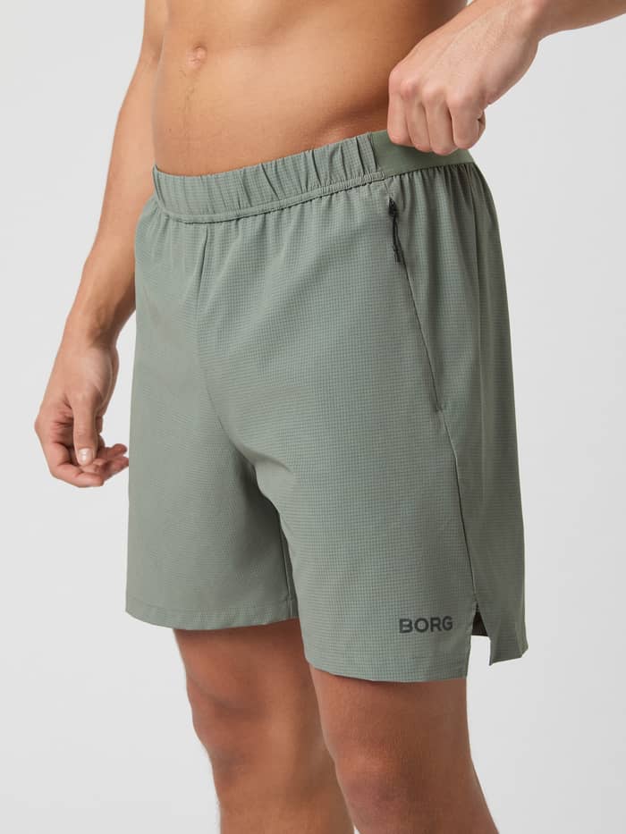 Side view of a model wearing the Borg Zip 7" Shorts in Agave Green, highlighting the fit and zippered pocket.