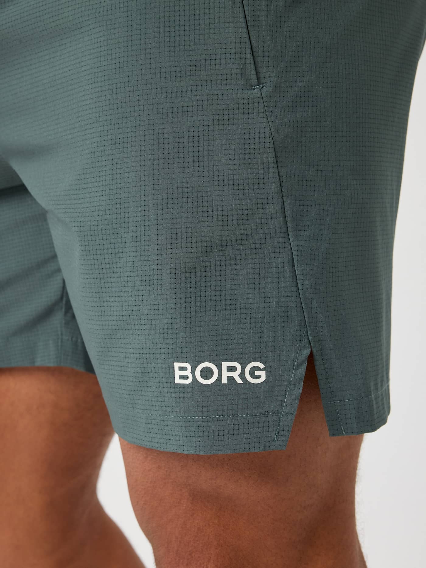 Close-up of the perforated Borg Zip Shorts 7 Inch in Urban Chic (Green), with a white logo and side slits for training. - Image 5